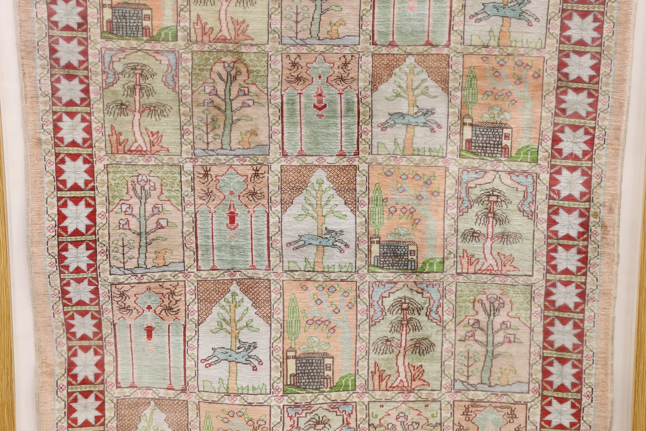 An Eastern framed silk rug depicting trees amimals and buildings, 86 cms high x 67cms wide